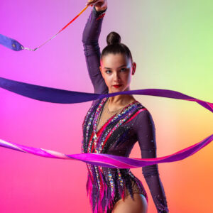 Half length portrait of one young rhythmic gymnast posing with ribbon in her hand isolated over bright multicolored neon background. Concept of sport life, motion, flexibility.